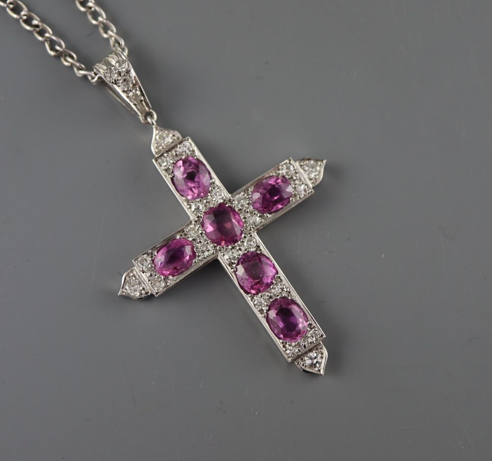 A white metal, six stone pink sapphire and diamond chip set cross pendant, on a white metal chain
